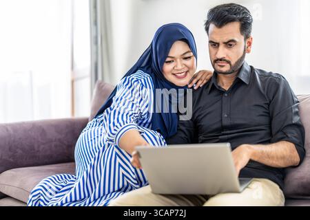 Muslim Couple using laptop Together on Sofa at Home Stock Photo