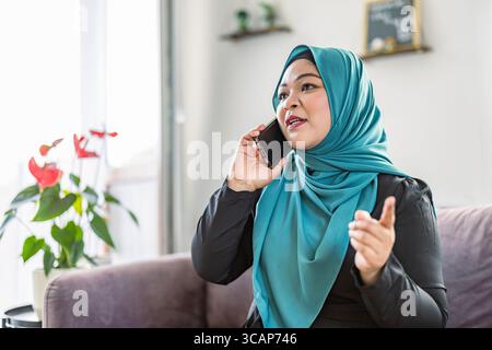 Happy muslim woman using mobile phone at home Stock Photo