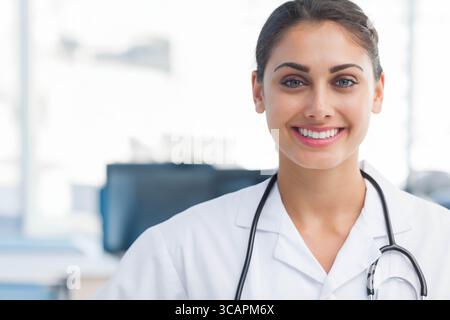 Smiling female doctor wearing lab coat and stethoscope in clinic with computer monitors, copy space Stock Photo