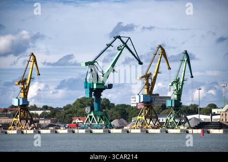 A scenic view showcases vibrant industrial cranes against a backdrop of a serene lake and a cloudy sky. Stock Photo