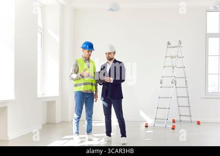 Two construction engineers in hard hats are talking in an empty house Stock Photo