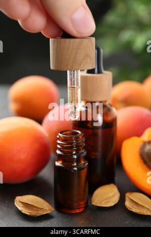 Woman dripping apricot essential oil from pipette into bottle at dark textured table, closeup Stock Photo