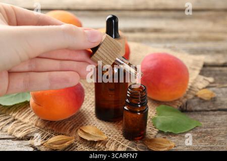 Woman dripping apricot essential oil from pipette into bottle at wooden table, closeup Stock Photo
