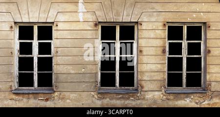 Three wooden white windows in the yellow plastered wall of a ruined old brick house. Glass isolated on black with patch. Panoramic collage from severa Stock Photo