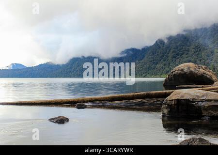 Tranquil Lake Landscape with Misty Forest Mountains and Rocks in the Foreground Stock Photo
