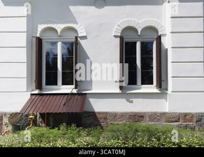Two windows in a small unknown church. The base is made of granite blocks, the wall is plastered with white paint Stock Photo