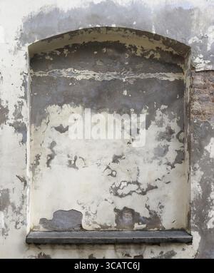The window in the wall of the old church was laid with bricks and plaster. The wall is covered with large spots and cracks Stock Photo