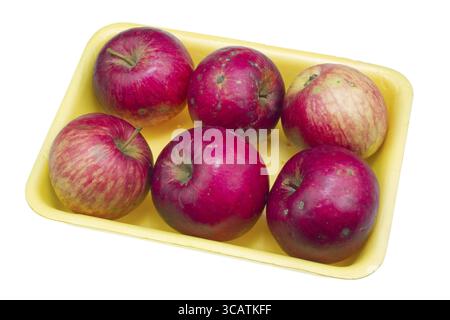 Cheap red ugly apples of the lowest price category for poor people in yellow plastic container. Isolated with patch Stock Photo