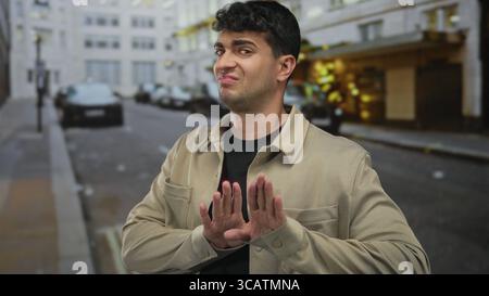 Man raises hands to stop on street while young hispanic urban guy shows clear gesture with open palms. Stock Photo