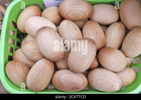 Homemade simple rustic wooden Easter eggs lie in a green plastic basket. Outdoor springtim e fair shot Stock Photo