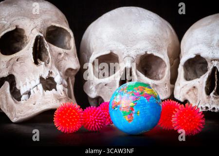 Coronavirus Covid-19 concept. Red virus Coronavirus models near world map globe and skulls against black background. Stock Photo