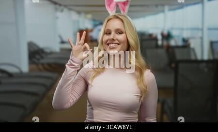 Young blonde woman with bunny ears makes an ok gesture while smiling on a cruise ship deck, exuding a funny and playful vibe amidst a relaxing environ Stock Photo