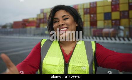 Woman smiling in reflective vest at a port with containers in the background, capturing a vibrant moment of joy and positivity at a bustling shipping Stock Photo