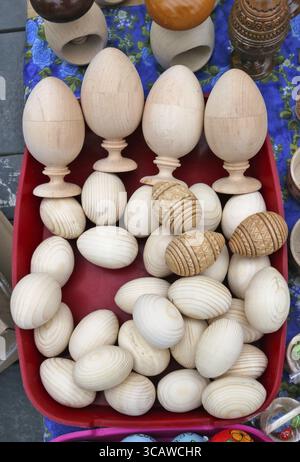 Homemade simple rustic wooden Easter eggs lie in a red plastic basket. Outdoor springtime fair shot Stock Photo
