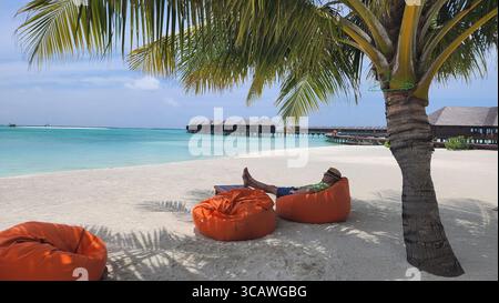 person relaxing on beanbag under palm trees on a tropical island in the maldives Stock Photo