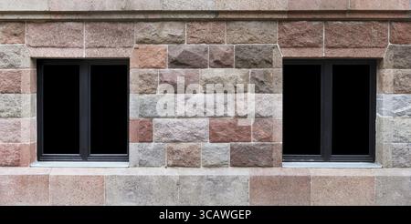 In a building wall from large red granite blocks there is a two windows. Glass isolated on black with patch Stock Photo