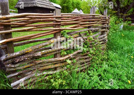Traditional fence made from logs and branches and wooden houses in the background in the Ethnographic Park in Cluj-Napoca. Romanian folk craftsmanship Stock Photo