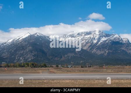 Snow-covered mountains from Grand Teton National Park rise majestically in the background under a clear blue sky from the Jackson Airport Runway JAC Stock Photo