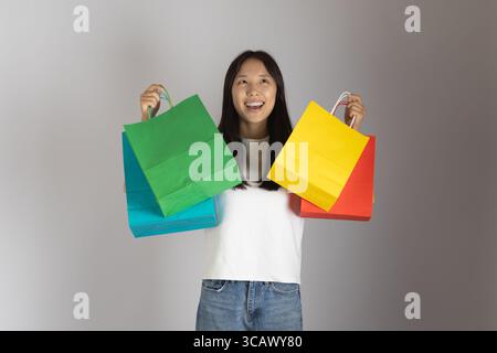 A joyful young woman beams, holding vibrant shopping bags in each hand one a striking green and blue Stock Photo