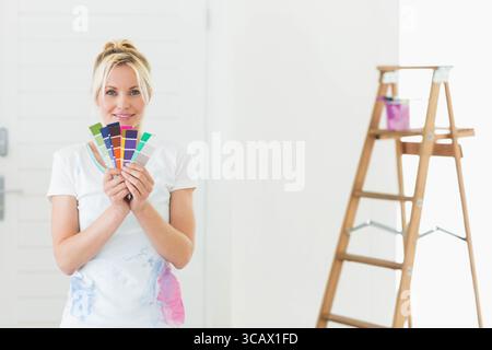 Woman holding paint swatches and selecting color in painted room with ladder and bucket Stock Photo