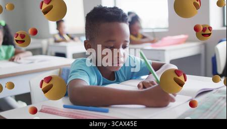 Writing boy wearing T-shirt using green pencil on open notebook at school desk, with ruler pen Stock Photo