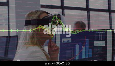 Woman wearing blazer and VR headset analyzing data using dual monitors at office desk, copy space Stock Photo