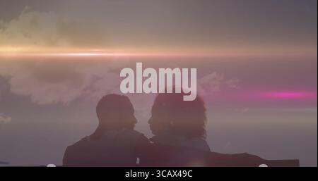 Hugging couple silhouette sitting on wooden bench at seaside viewpoint, pastel sunset sky Stock Photo