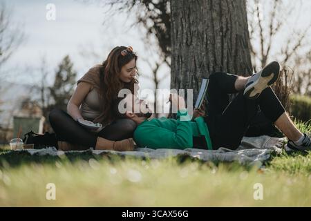 Young couple resting on a picnic blanket under a tree outdoors Stock Photo