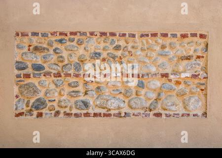 Light brown plastered wall with red brick inserts in rows and large river stones cemented in exposed view. Graphic element for background and texture, Stock Photo