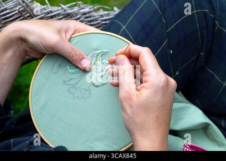 Woman holding needle thread hands embroidery green fabric textile craft Stock Photo