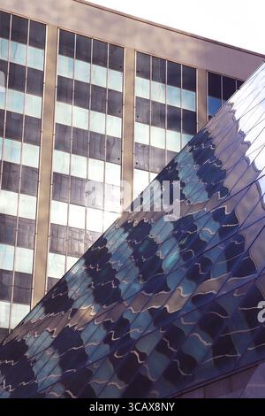 Two buildings meeting at a sharp diagonal line with grid pattern of rectangular windows reflecting in glass surface of the diagonal building Stock Photo