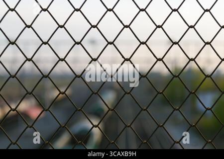 Cells of a wire fence in the evening against the background of a railway in a blur Stock Photo