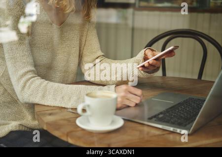 woman Caucasian faceless working on a laptop on the table. Woman in denim shirt does telework at home. Concept teleworking and remote work. High quali Stock Photo