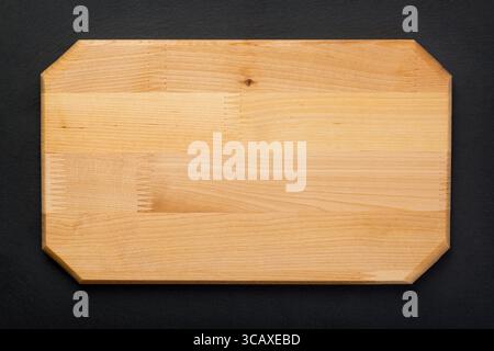 New rectangular wooden cutting board on on black stone slate plate. Mockup for food project. Top view. Stock Photo