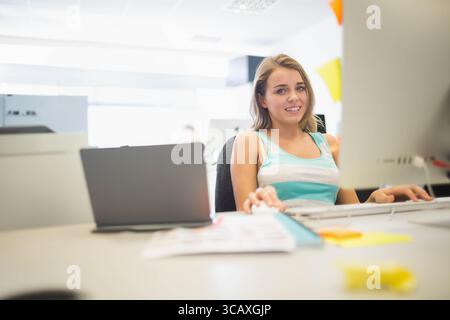 Female office worker working on laptop and monitor at office desk with sticky notes, copy space Stock Photo