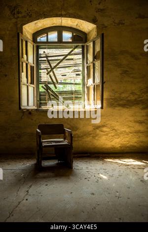 Sunlit abandoned room with broken window and old wooden chair, showcasing rustic decay and urban exploration atmosphere Stock Photo