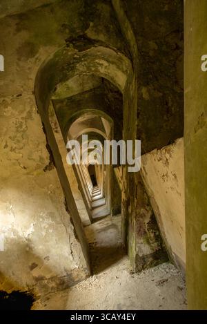 Mysterious narrow corridor with repeating arches in an abandoned, decaying building covered with moss and peeling paint Stock Photo