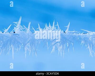 Close-up of sharp frost crystals forming on a wire against a clear blue winter sky in Switzerland Stock Photo