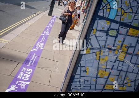 A phone user and other pedestrians walk past pavement messages on Oxford Street that warn them of the increasing trend of phone snatch crime, the 'Mind the Grab' initiative by Westminster, the Met Police and the Currys retailer, on 7th August, 2025, in London, England. Statistics reveal that in 2024, a phone was stolen every 15 minutes in Westminster - 94 a day and over 34,000 in total. Typically, these thefts involve criminals on mopeds or e-bikes snatching phones straight from people’s hands on busy pavements. Stock Photo