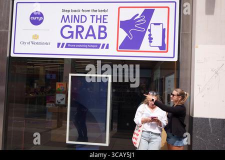 A phone user and other pedestrians walk past messages on Oxford Street that warn them of the increasing trend of phone snatch crime, the 'Mind the Grab' initiative by Westminster, the Met Police and the Currys retailer, on 7th August, 2025, in London, England. Statistics reveal that in 2024, a phone was stolen every 15 minutes in Westminster - 94 a day and over 34,000 in total. Typically, these thefts involve criminals on mopeds or e-bikes snatching phones straight from people’s hands on busy pavements. Stock Photo
