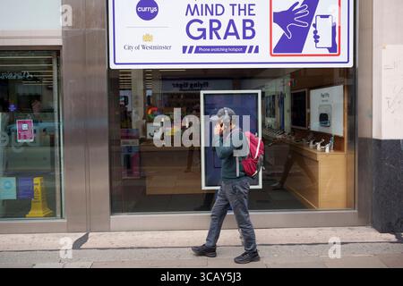 A phone user and other pedestrians walk past messages on Oxford Street that warn them of the increasing trend of phone snatch crime, the 'Mind the Grab' initiative by Westminster, the Met Police and the Currys retailer, on 7th August, 2025, in London, England. Statistics reveal that in 2024, a phone was stolen every 15 minutes in Westminster - 94 a day and over 34,000 in total. Typically, these thefts involve criminals on mopeds or e-bikes snatching phones straight from people’s hands on busy pavements. Stock Photo