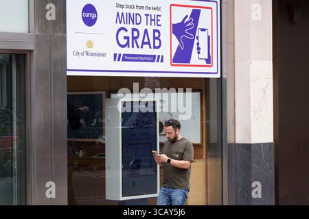 A phone user and other pedestrians walk past messages on Oxford Street that warn them of the increasing trend of phone snatch crime, the 'Mind the Grab' initiative by Westminster, the Met Police and the Currys retailer, on 7th August, 2025, in London, England. Statistics reveal that in 2024, a phone was stolen every 15 minutes in Westminster - 94 a day and over 34,000 in total. Typically, these thefts involve criminals on mopeds or e-bikes snatching phones straight from people’s hands on busy pavements. Stock Photo