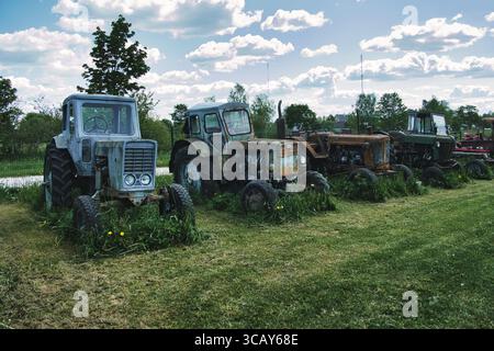 Row of Abandoned Vintage Tractors on Overgrown Farm Field Stock Photo