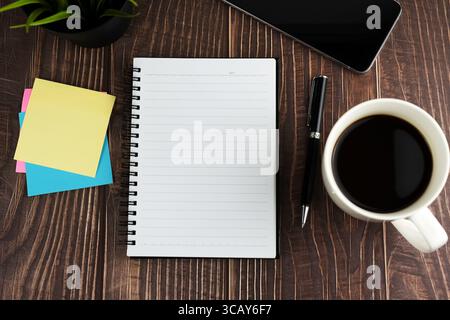 Top view of blank notepad, adhesive note, cup of coffee on wood table Stock Photo