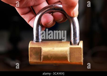 Hand holding a brass padlock on a dark background. Stock Photo