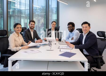 Group of five diverse professionals engaging in a corporate meeting around a table. Discussing documents and ideas in a collaborative and contemporary workspace Stock Photo