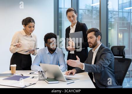 A group of diverse professionals is discussing work at an office desk, actively engaging and focusing on their collaborative tasks. Stock Photo