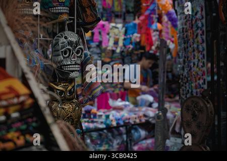 Handcrafted skull and owl figurines on display at La Ciudadela Artisan Market in Mexico City, surrounded by colorful traditional textiles Stock Photo