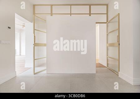 Contemporary walk-in closet design with high-gloss white doors and satin-finished metal entrances with frosted glass Stock Photo