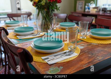 Dining table with chairs close up set with fresh flowers in vase plates bowls silverware and drinking glasses. Stock Photo
